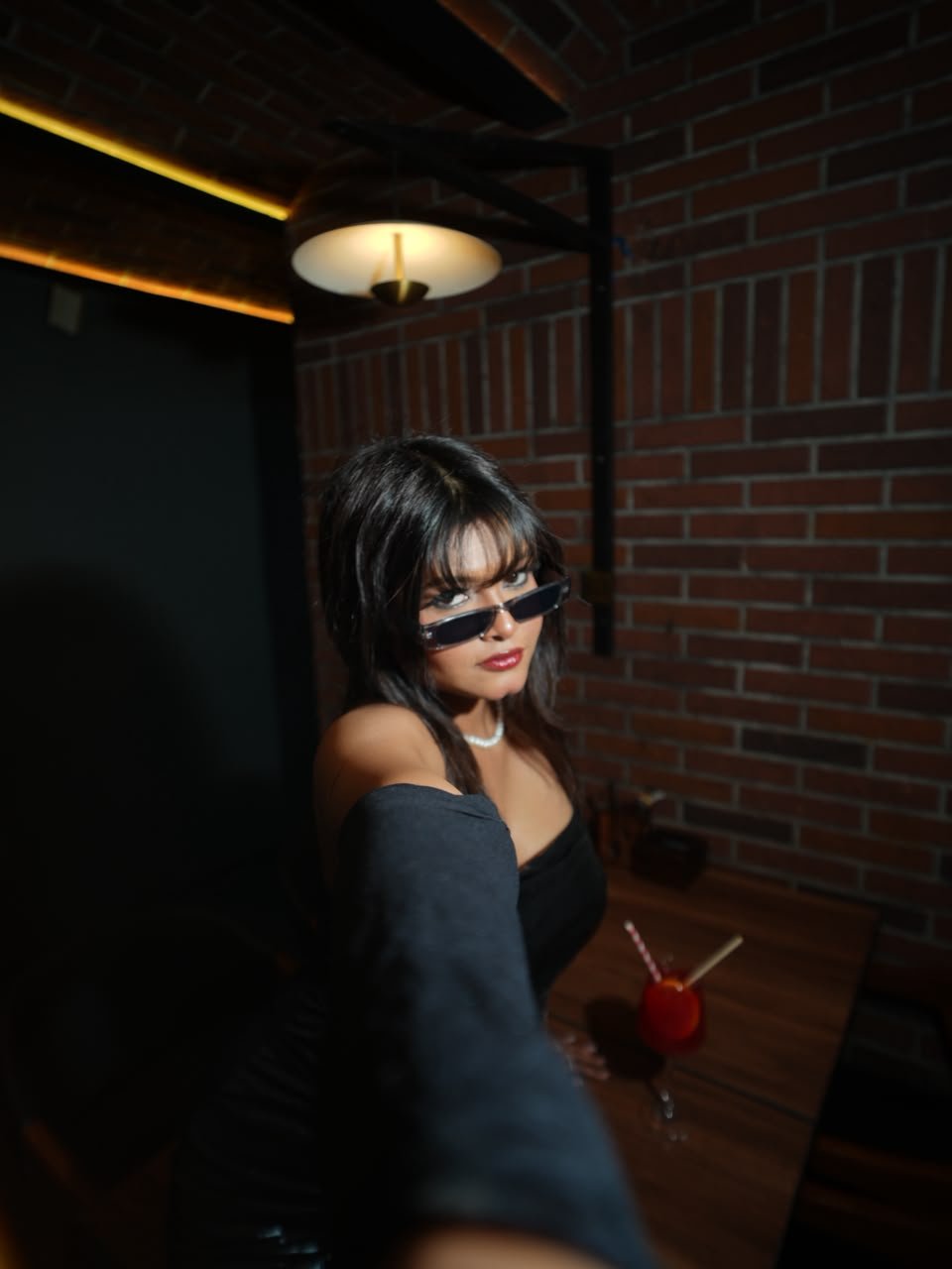 Vaishnavi Kadekar in sunglasses and a black off-shoulder top at a brick-walled lounge